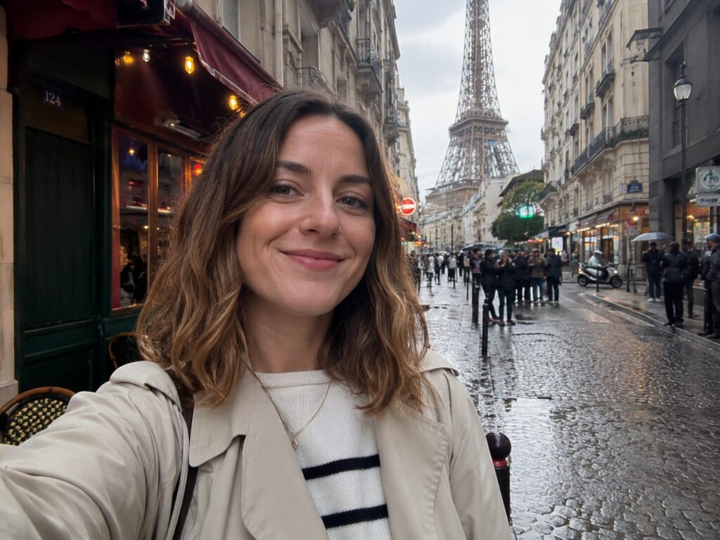 A woman smiling at the camera on a wet cobblestone street in Paris with the Eiffel Tower visible behind her